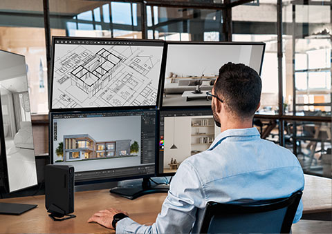 İki monitörlü tasarım bilgisayarı ve mimari çizimlerle iç mimarlık ve 3D modelleme çalışmalarını gösteren modern ofis ortamı.