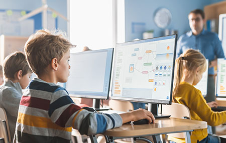 Çocukların bilgisayar başında eğitim aldığı modern okul sınıfı, teknolojik öğrenme ortamı ve dijital eğitim araçları.