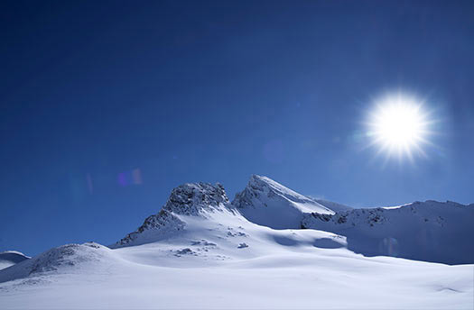 Dağlık alanda karla kaplı tepe ve parlak güneşli gökyüzü, kış doğa manzarası.